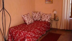 A bedroom with a floral bedspread, a small bedside table with a lamp, and a painting on the wall.