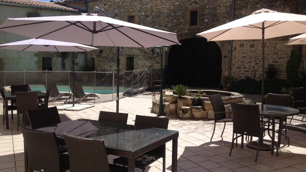 An outdoor patio with wicker furniture, stone walls, and a pool.