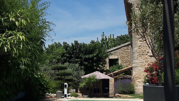 A swimming pool with a stone building in the background, surrounded by greenery. -  comfortable cottages in character farmhouse located in Drôme Provençal (Grillon)