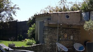 A backyard with a stone wall, a small building, and two lounge chairs. -  comfortable cottages in character farmhouse located in Drôme Provençal (Grillon)