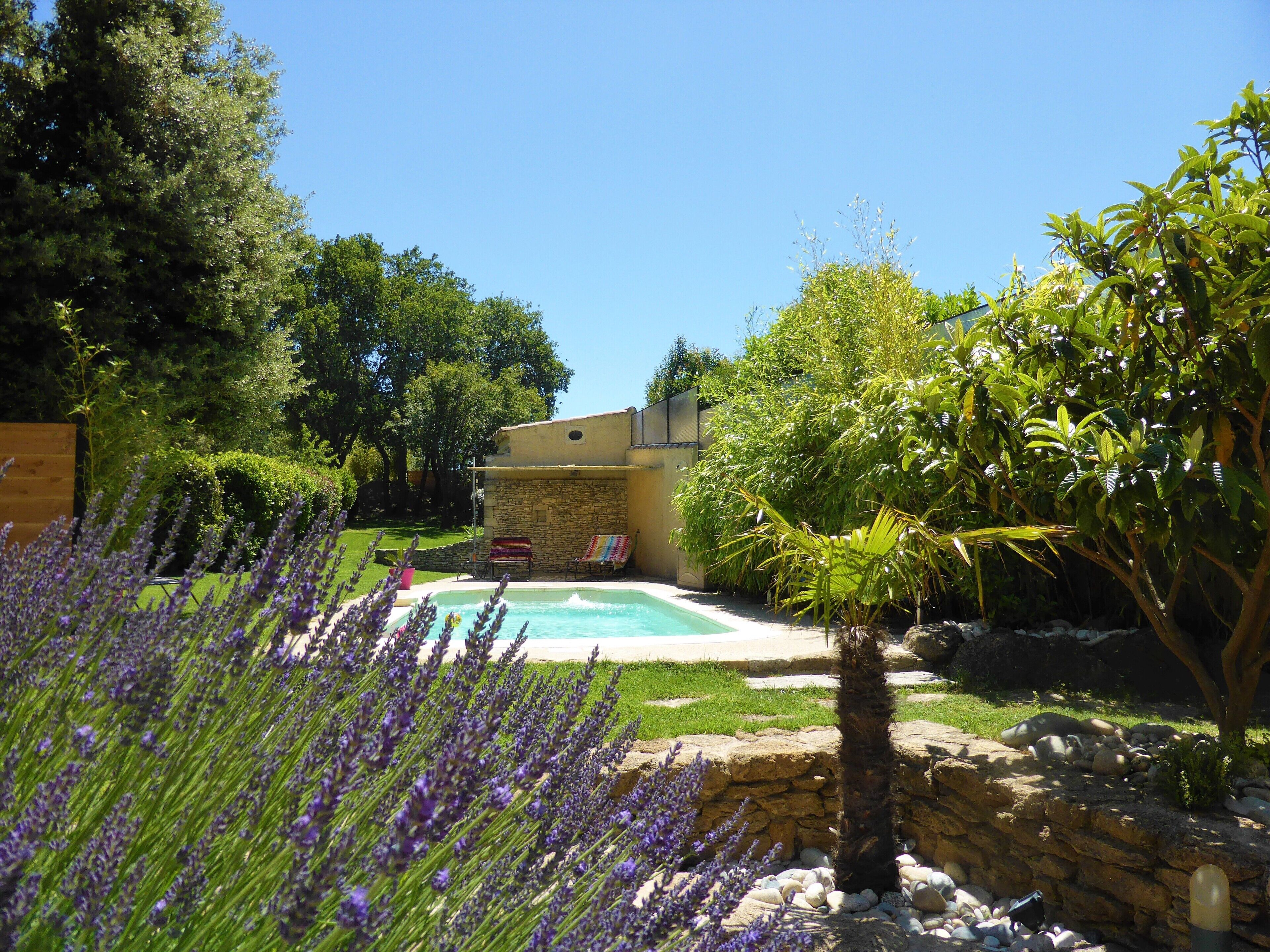 Une piscine entourée d’un jardin agrémenté de lavande, d’un mur de pierre et d’un bâtiment à la façade en pierre.