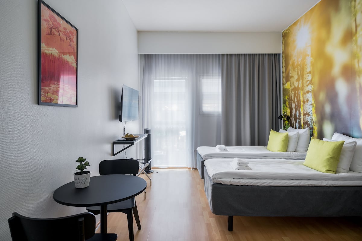 A hotel room with two beds, a desk with a chair, a small table, and a TV on a stand.
