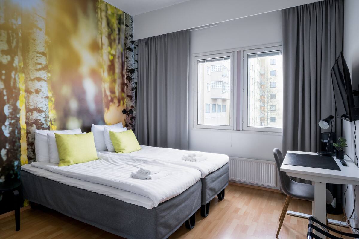 A modern hotel room with a large bed, a desk, and a view of the city through the window.