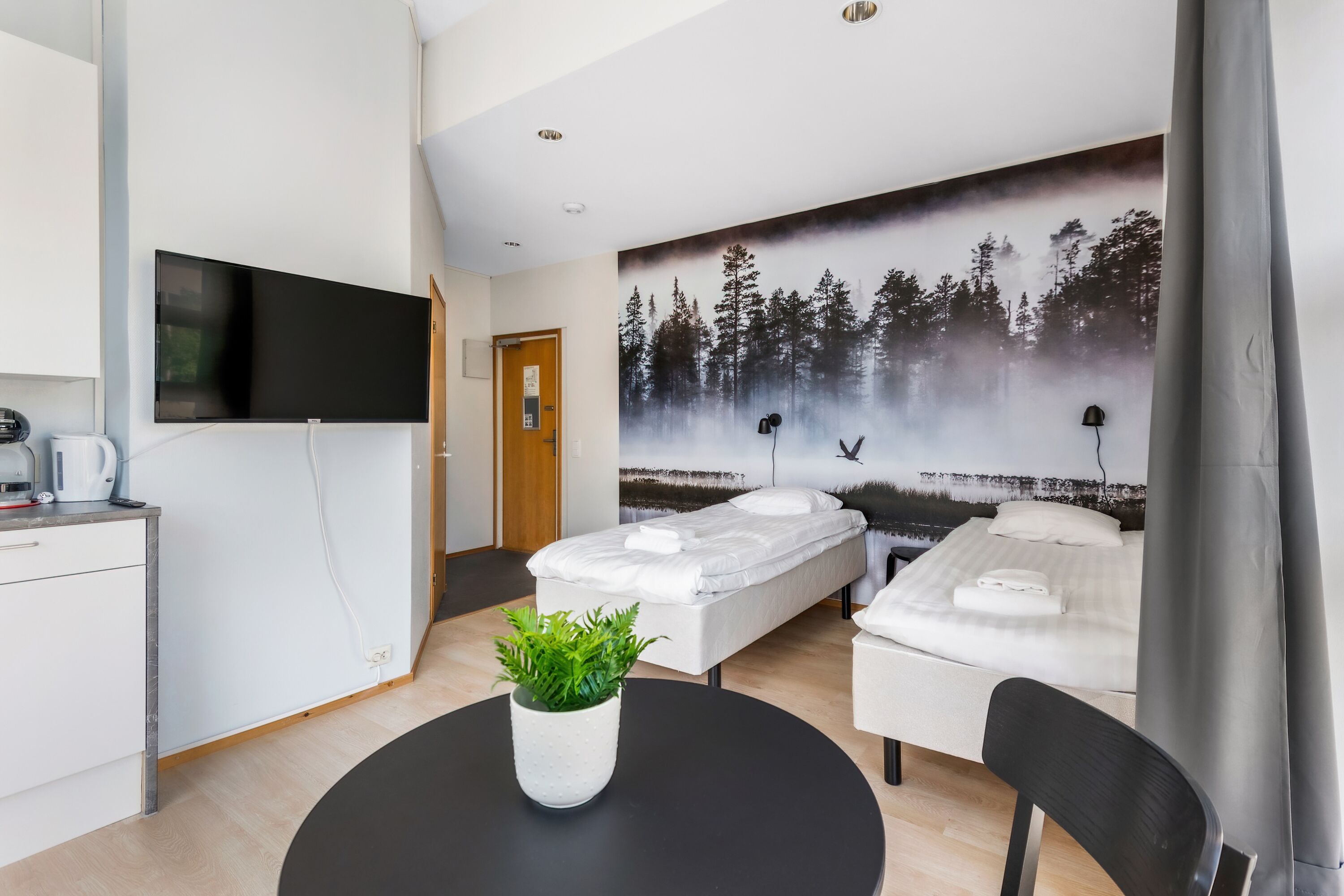 Quarto de hotel moderno com cama, escrivaninha, cadeira e televisão.