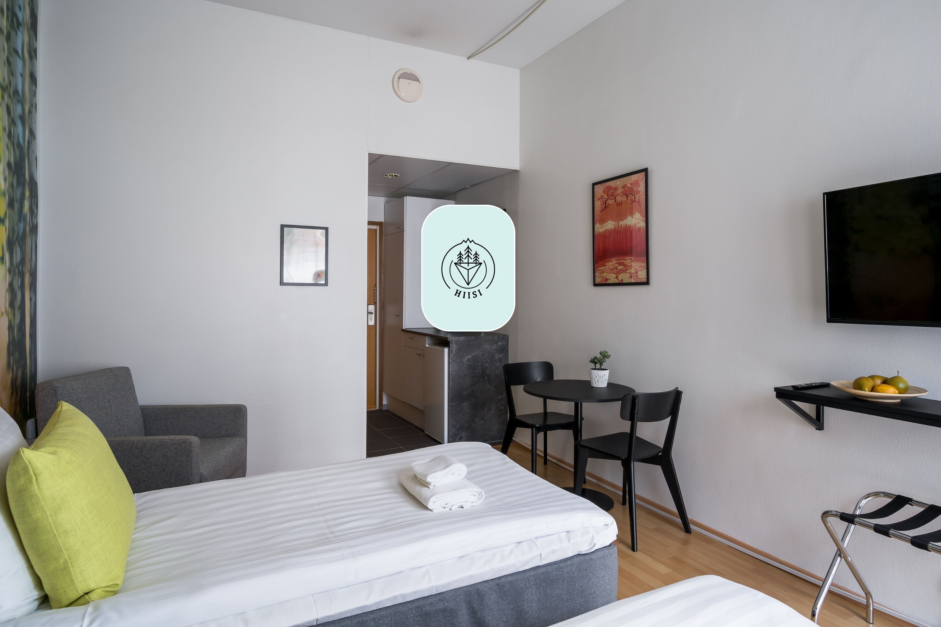 Een moderne hotelkamer met een bed, een bureau, een stoel, een televisie en een klein tafeltje met fruit.