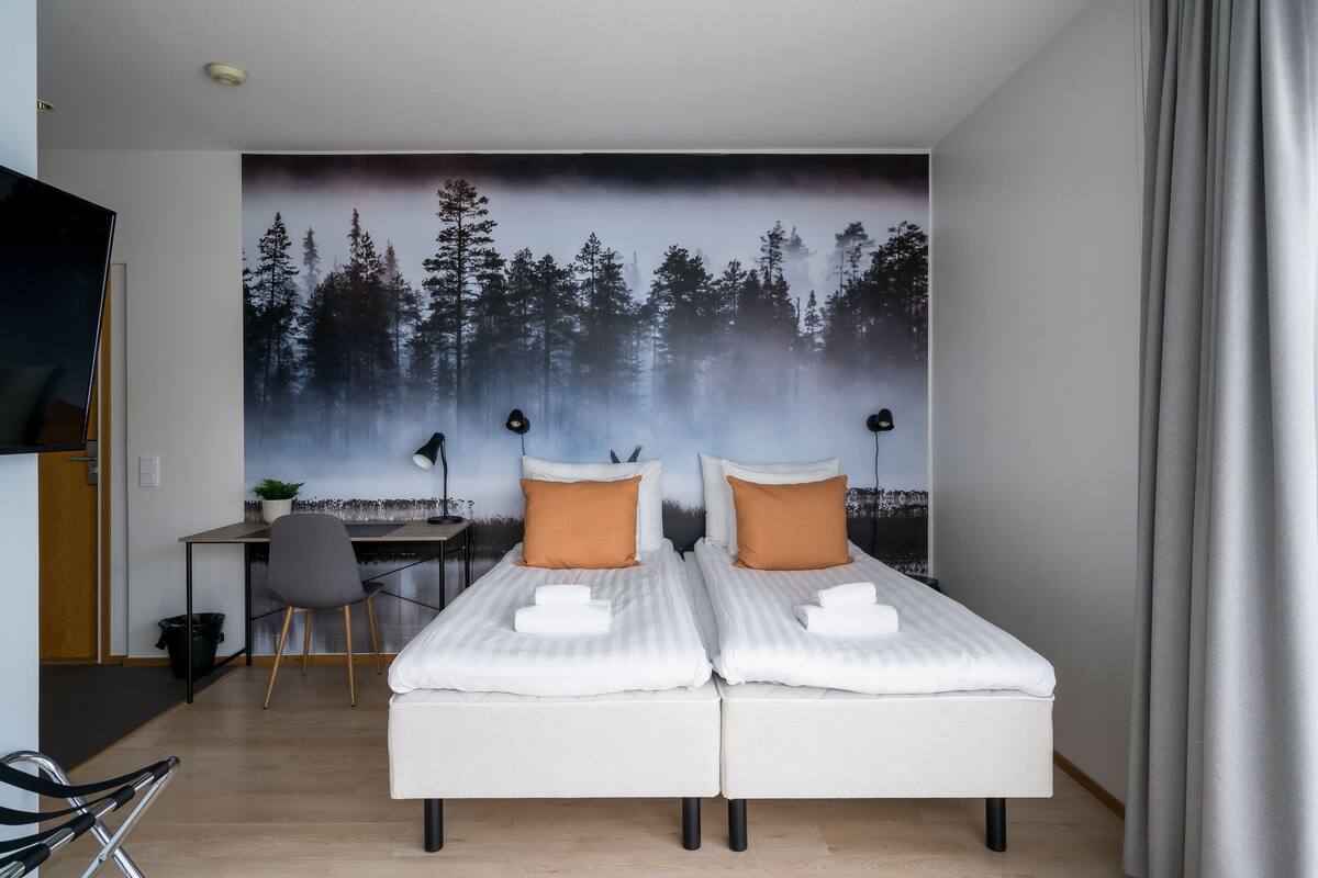A modern bedroom with two beds, a desk, and a chair.