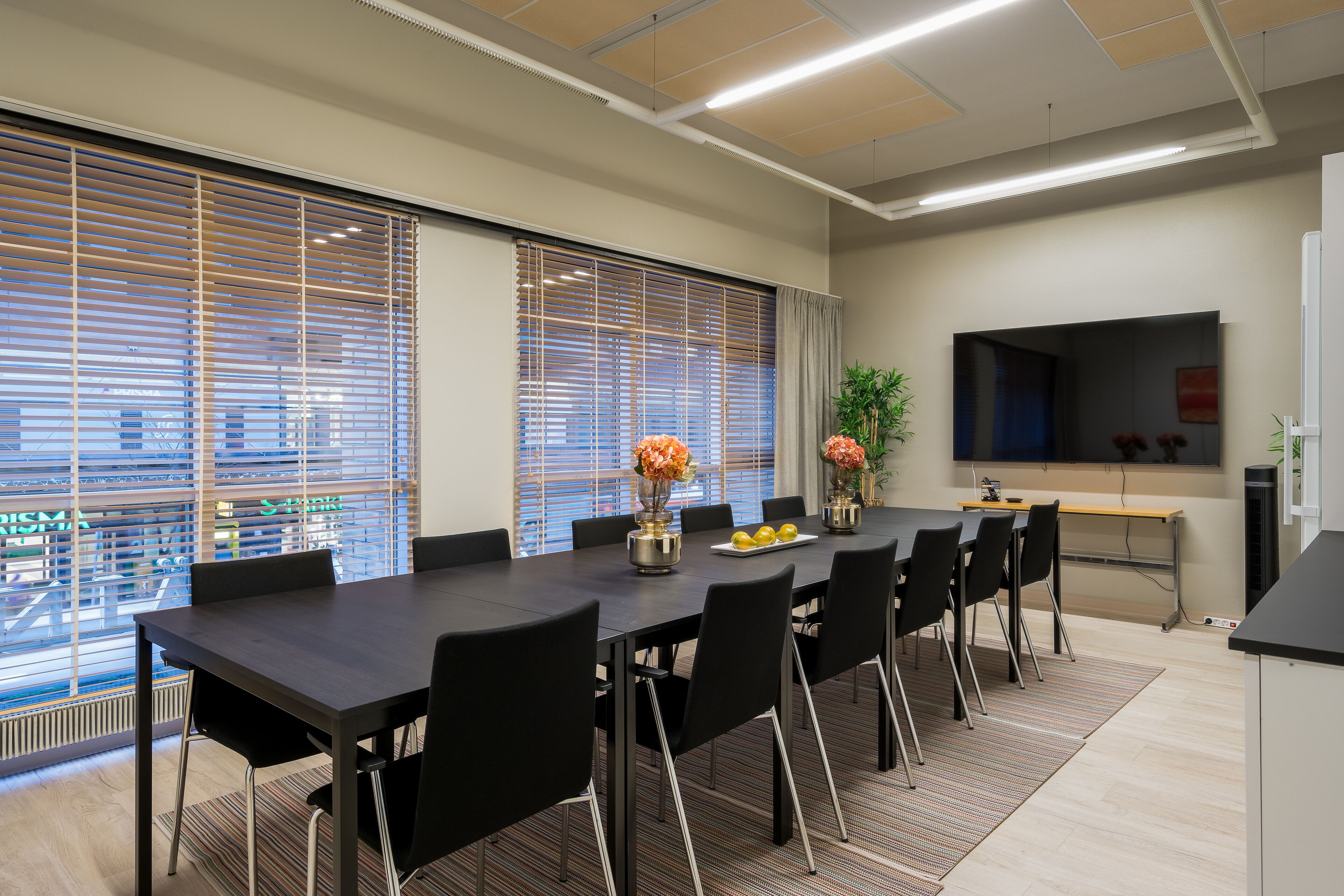 A conference room with a long table, black chairs, and large windows with blinds.