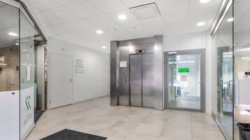 Un área de ascensor moderna con puerta de vidrio, cabina metálica y suelo de baldosas.