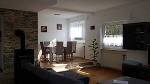 Una sala de estar con chimenea, un comedor con mesa y sillas, y un ventanal con vistas a árboles.