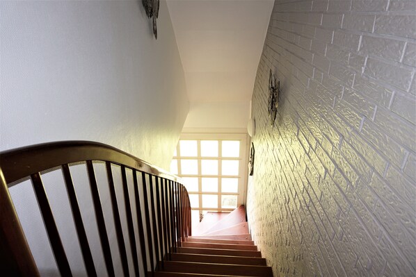 Un escalier avec une rampe en bois menant à une porte ornée d’un motif à carreaux.