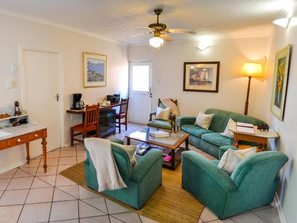 Una sala de estar con un sofá verde, una mesa de centro, un comedor con una silla y una mesa, y un ventilador de techo.