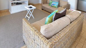 A spacious living area with a wicker sofa, a television on a white stand, and artwork on the walls. - Sundune Guest House & Self Catering (Colchester)
