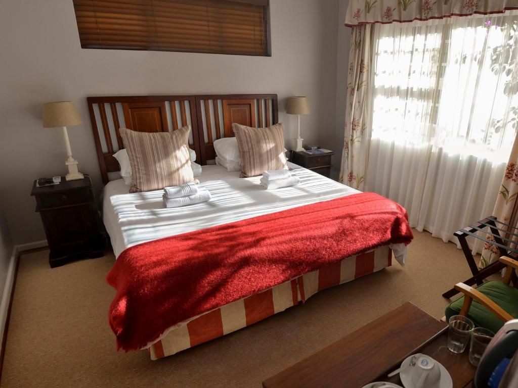 A neatly made bed with a red blanket, two bedside tables with lamps, and a window with curtains.
