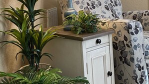 Ein Zimmer mit einer Couch, einer Lampe, einem kleinen Schrank und einer Topfpflanze.