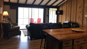 Ein gemütliches Zimmer mit Holzbalkendecke, einem Esstisch mit Stühlen, einer Couch und einem an der Wand montierten Fernseher.