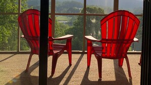 Ein Balkon mit zwei roten Stühlen und einem Tisch, mit Blick auf eine malerische Seen- und Berglandschaft.