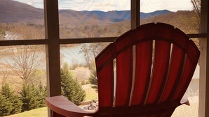 Ein roter Adirondack-Sessel mit Blick auf eine Landschaft mit See und Bergen, durch große Fenster.