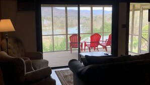 Ein gemütliches Wohnzimmer mit einem großen Fenster mit Blick auf eine malerische Landschaft, ausgestattet mit einer Couch, Sesseln und roten Stühlen.