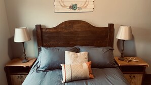 Een slaapkamer met een houten hoofdbord, een blauw beddegoed en twee nachtkastjes met lampen en decoratieve objecten.
