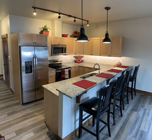 A modern kitchen with a central island, stainless steel appliances, and wooden flooring.