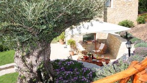 Un espace extérieur aménagé en terrasse, avec un mur en pierre, un grand parasol et du mobilier de jardin.