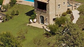 Un bâtiment en pierre doté d’une piscine, entouré d’une pelouse et de quelques chaises longues.