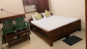 A room with a bed, two green chairs, a small table, a window with curtains, and a wall-mounted air conditioner. - Hotel Anjali (Deoghar)