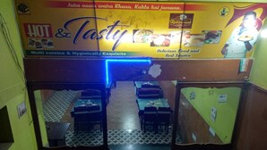 An interior view of a restaurant with a signboard advertising 'HOT & CUSTY' cuisine, a tiled floor, and tables set for dining. - Hotel Anjali (Deoghar)