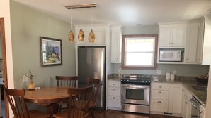 Una cocina con sillas de madera, una mesa de comedor, un refrigerador, un horno, un microondas y armarios.