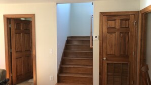 Una escalera de madera en un pasillo con paredes de tonos claros y una lámpara en el techo.