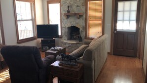 Una sala de estar con chimenea de piedra, piso de madera, televisor, sofá y sillón.
