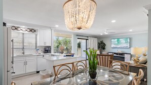 A modern kitchen with white cabinets, a dining area with a glass table, and a chandelier.