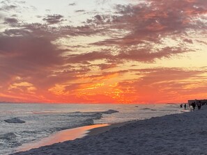 A beach with a sunset, waves, and people walking.