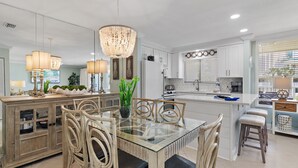 A modern kitchen with white cabinetry, a glass-top dining table, wicker chairs, and pendant lighting.