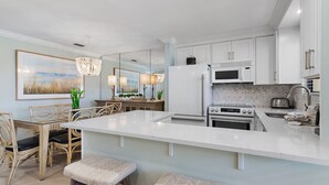 A modern kitchen with white cabinetry, a large island, and a dining area with wicker chairs and a chandelier.
