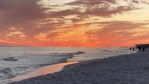 A beach with a sunset, waves, and people walking.