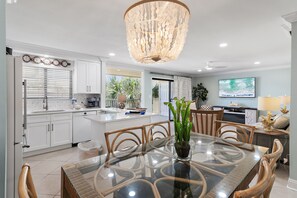 A modern kitchen with white cabinets, a dining area with a glass table, and a chandelier.