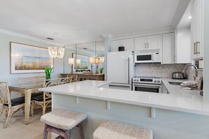 A modern kitchen with white cabinetry, a large island, and a dining area with wicker chairs and a chandelier.