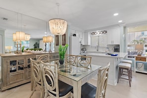 A modern kitchen with white cabinetry, a glass-top dining table, wicker chairs, and pendant lighting.