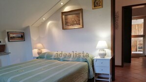 A bedroom with a bed, two bedside tables with lamps, a wall-mounted painting, and a door leading to another room. - cozy attic in Dervio (dervio)