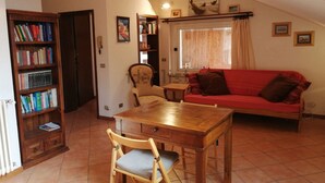 A cozy living room with a wooden table, a red sofa, and a bookshelf filled with books. - cozy attic in Dervio (dervio)