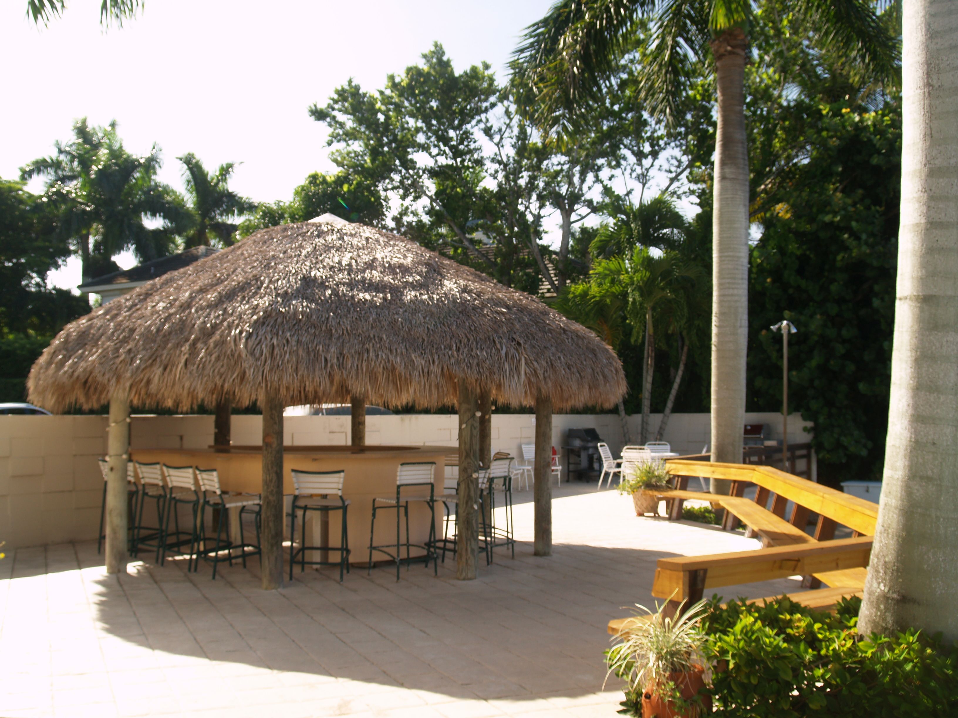 Un'area salotto all'aperto con ombrellone di paglia, sedie e panca in legno.