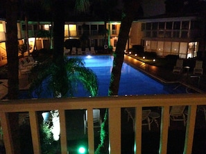 A nighttime view of a hotel pool area with lounge chairs and a palm tree.
