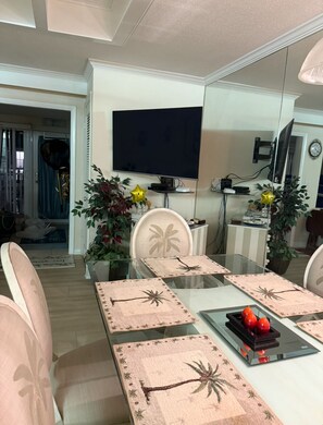 A dining area with a glass table, chairs, and a TV mounted on the wall.