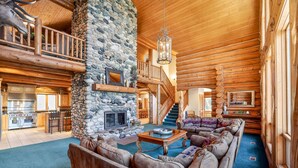 A log cabin interior with a stone fireplace, a wooden staircase, a living room with a sofa and coffee table, and a kitchen area. - Luxury Log Cabin Near Cascade Lake, 80 Acres, RVs (Cascade)