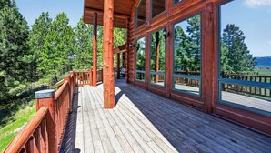 A wooden deck with railings, large windows, and a view of trees and mountains. - Luxury Log Cabin Near Cascade Lake, 80 Acres, RVs (Cascade)