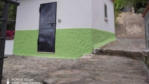 Een laag, enkelvoudig gebouw met een buitenkant in groen en wit, een zwarte deur en een klein raam.