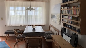 A dining area with a table, chairs, a bench, a bookshelf, and a ceiling fan.