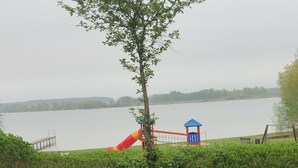A view of a lake with a playground, including a slide and a swing set, surrounded by lush greenery.