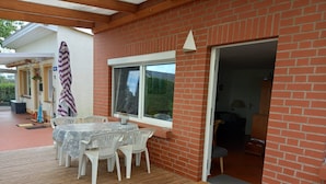 A covered patio with a table and chairs, a brick wall, and a door leading inside.